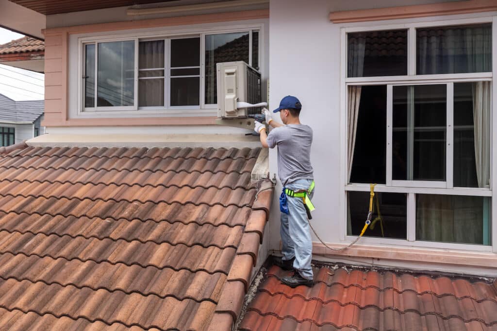 Technician fixing air conditioner unit on outside wall.